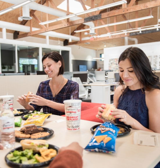 two women eating sandwiches while smiling