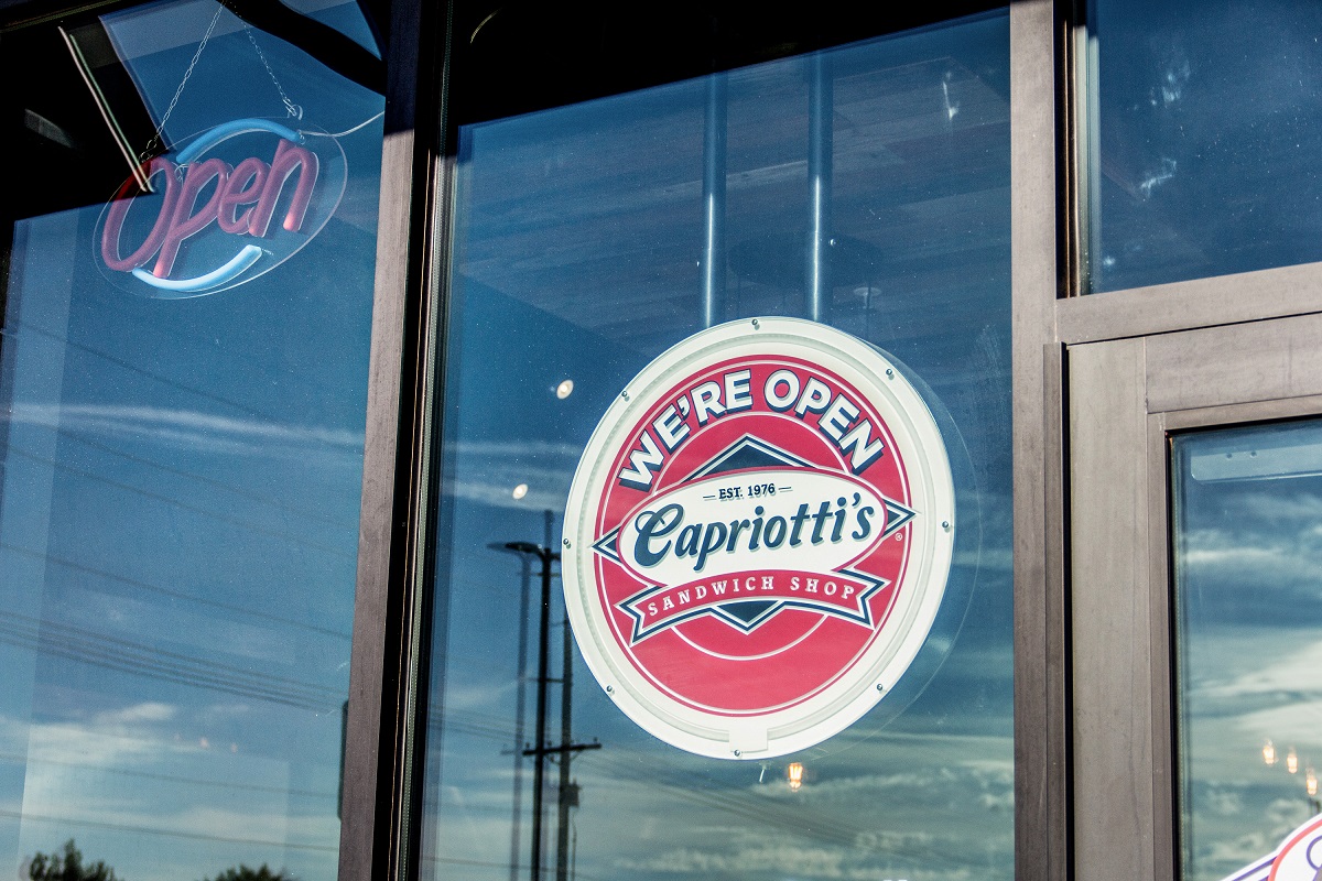 A sign in the window of Capriotti's that reads, "We're Open"